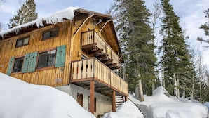 Un chalet en bois doté d’un balcon, entouré de neige et de grands pins.