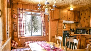 L’intérieur chaleureux d’un chalet avec une table à manger en bois, des bancs et un coin cuisine.