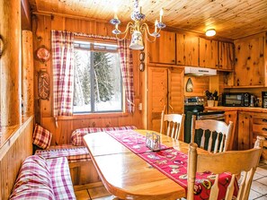 A cozy cabin interior with a wooden dining table, benches, and a kitchen area.