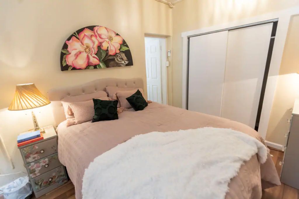 A bedroom with a bed, a nightstand, a dresser, a painting, and a wardrobe.