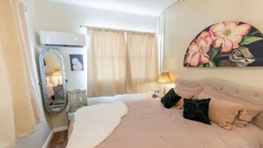 A bedroom with a bed, a mirror, a lamp, and a painting on the wall.