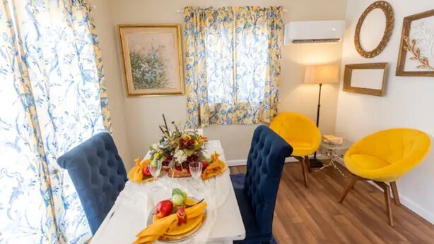A dining area with a table set for two, blue upholstered chairs, a yellow chair, and a floral centerpiece.