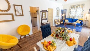 A dining area with a table set for four, a blue sofa, and a ceiling fan in a well-lit room with white walls and wooden flooring.