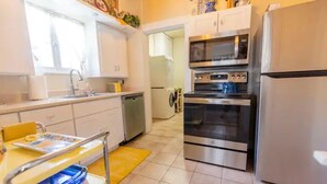 A modern kitchen with stainless steel appliances, a yellow dining table, and a view into the adjacent living area.
