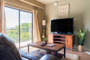 A living room with a large TV, a coffee table, a sofa, and a balcony with curtains. - Bohemian Austin Vibes 🤘 (Austin)