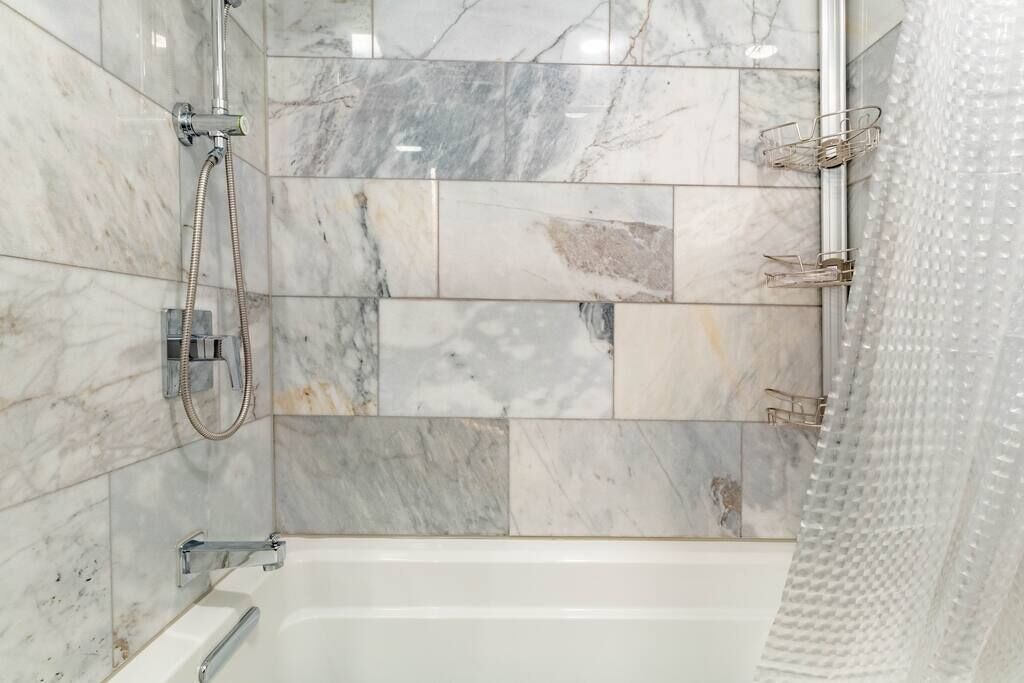 A bathroom with a bathtub, a shower, and a tiled wall with a marble pattern.