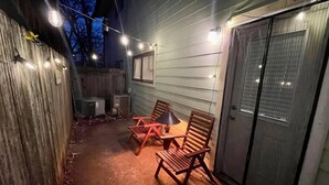 Un patio al aire libre con mesa y sillas de madera, luces colgantes y un área de estar cubierta.