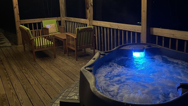 Un jacuzzi con iluminación azul, terraza de madera y mobiliario exterior.
