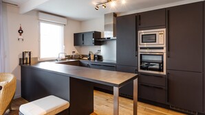 A modern kitchen with dark cabinetry, a large island, and built-in appliances. - Le ViLoNa - T3 moderne avec parking privé (Rennes)
