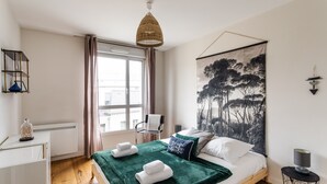 A bedroom with a bed, a window, a hanging light fixture, and a wall-mounted artwork. - Le ViLoNa - T3 moderne avec parking privé (Rennes)