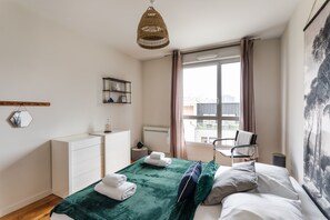 A modern bedroom with a bed, a dresser, a chair, a window with curtains, and a hanging light fixture. - Le ViLoNa - T3 moderne avec parking privé (Rennes)
