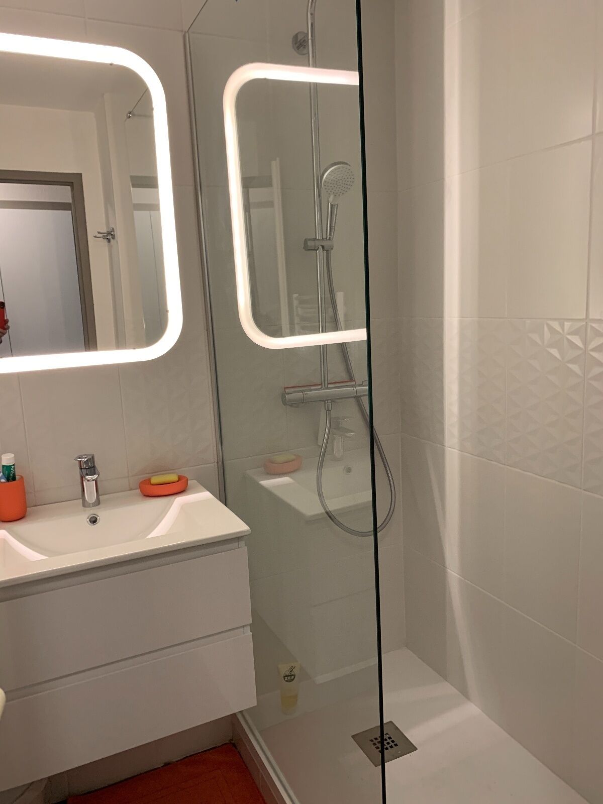 A modern bathroom with a glass-enclosed shower, a white sink with a mirror above it, and a red towel holder.
