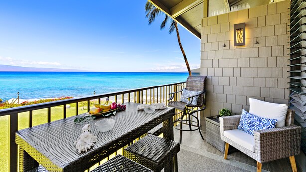 Ein Balkon mit Korbmöbeln, Blick auf das Meer und eine Backsteinmauer.