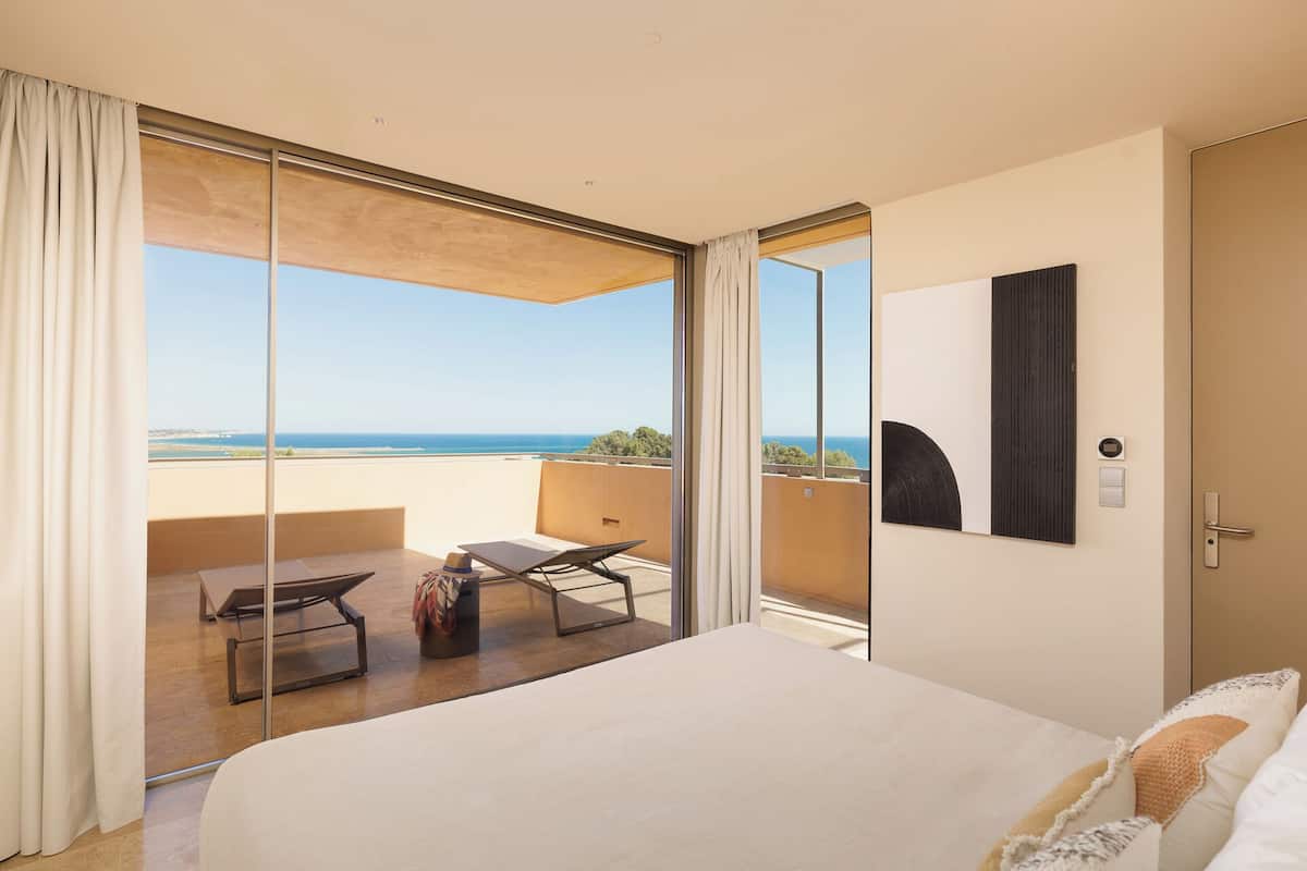 A hotel room with a large bed, a balcony with a view of the sea, and a modern design.