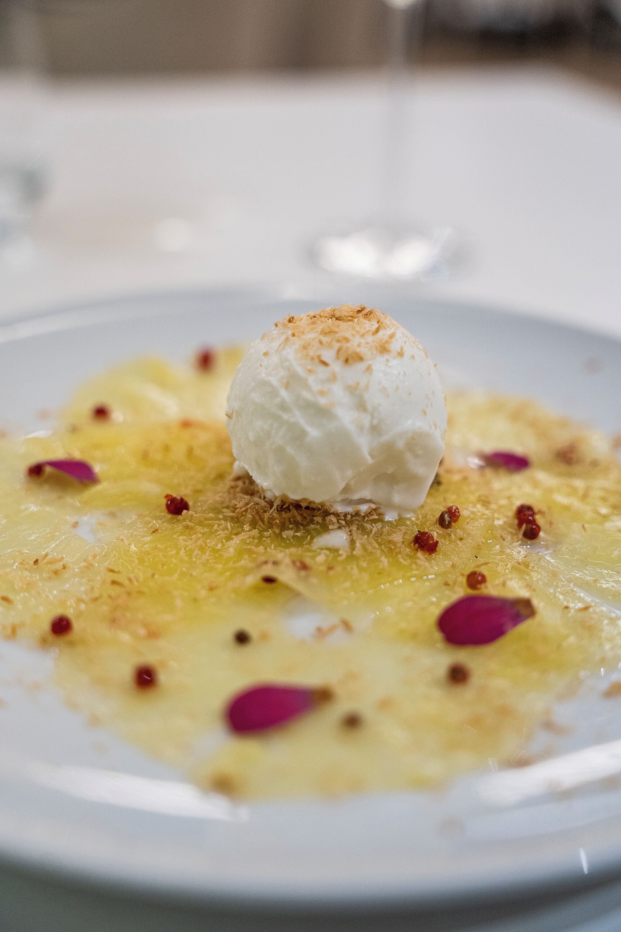 A dessert with a scoop of ice cream on a plate with a golden sauce and red garnish.