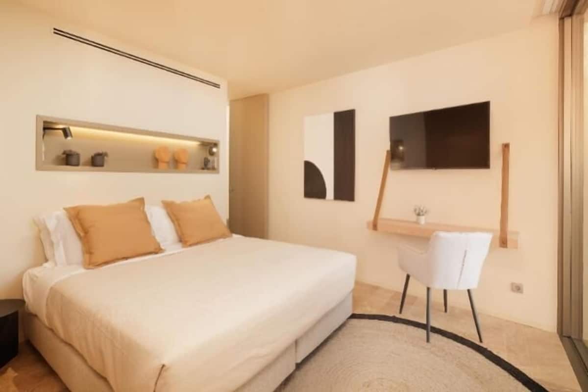 A modern bedroom with a large bed, a desk, and a chair.