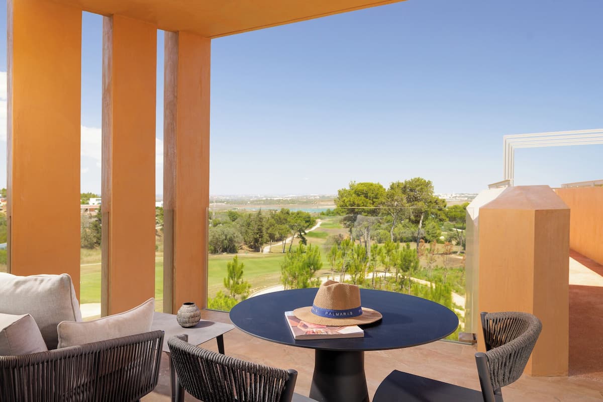 A balcony with a table, chairs, and a view of a green landscape.