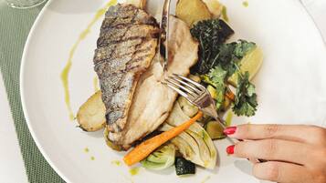 A plate of food with a grilled fish, vegetables, and a glass of white wine on a table.