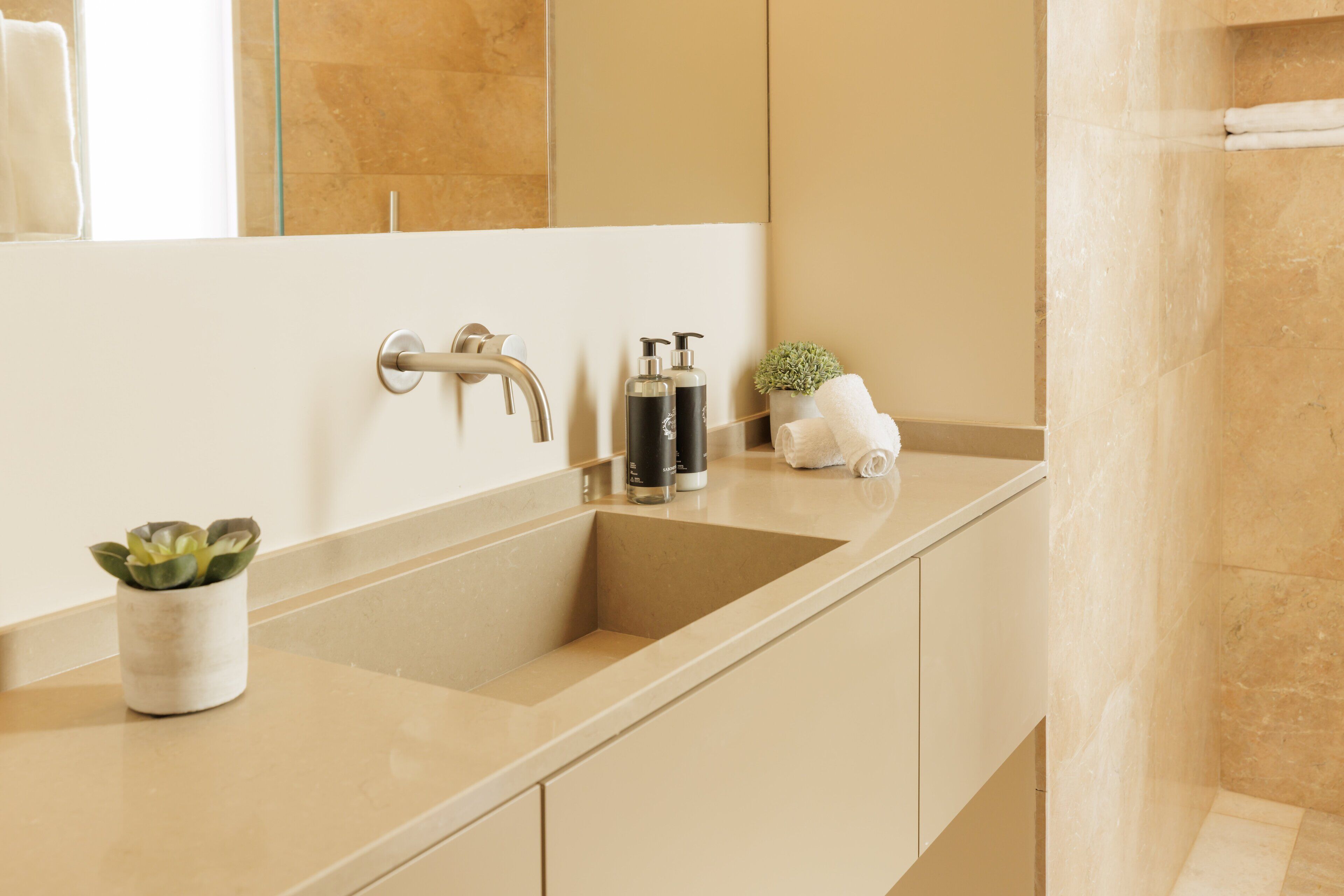 A modern bathroom with a large mirror, a sink, and a small plant.
