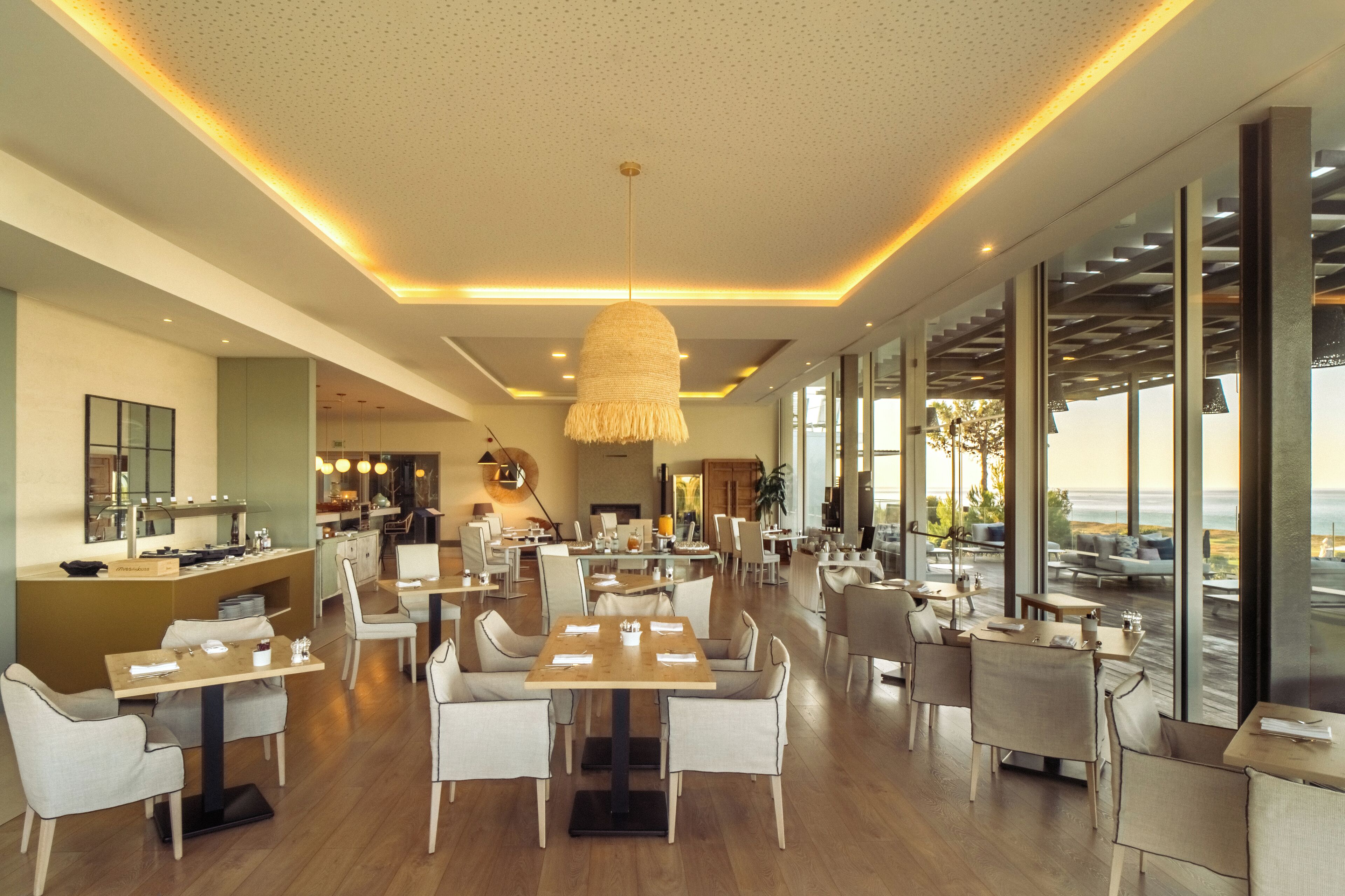 A modern restaurant with a central dining area, a bar, and large windows offering a view.