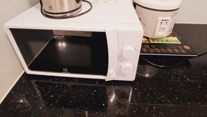 Um forno micro-ondas com uma chaleira em cima, um cozidinho de arroz e um painel de controle.