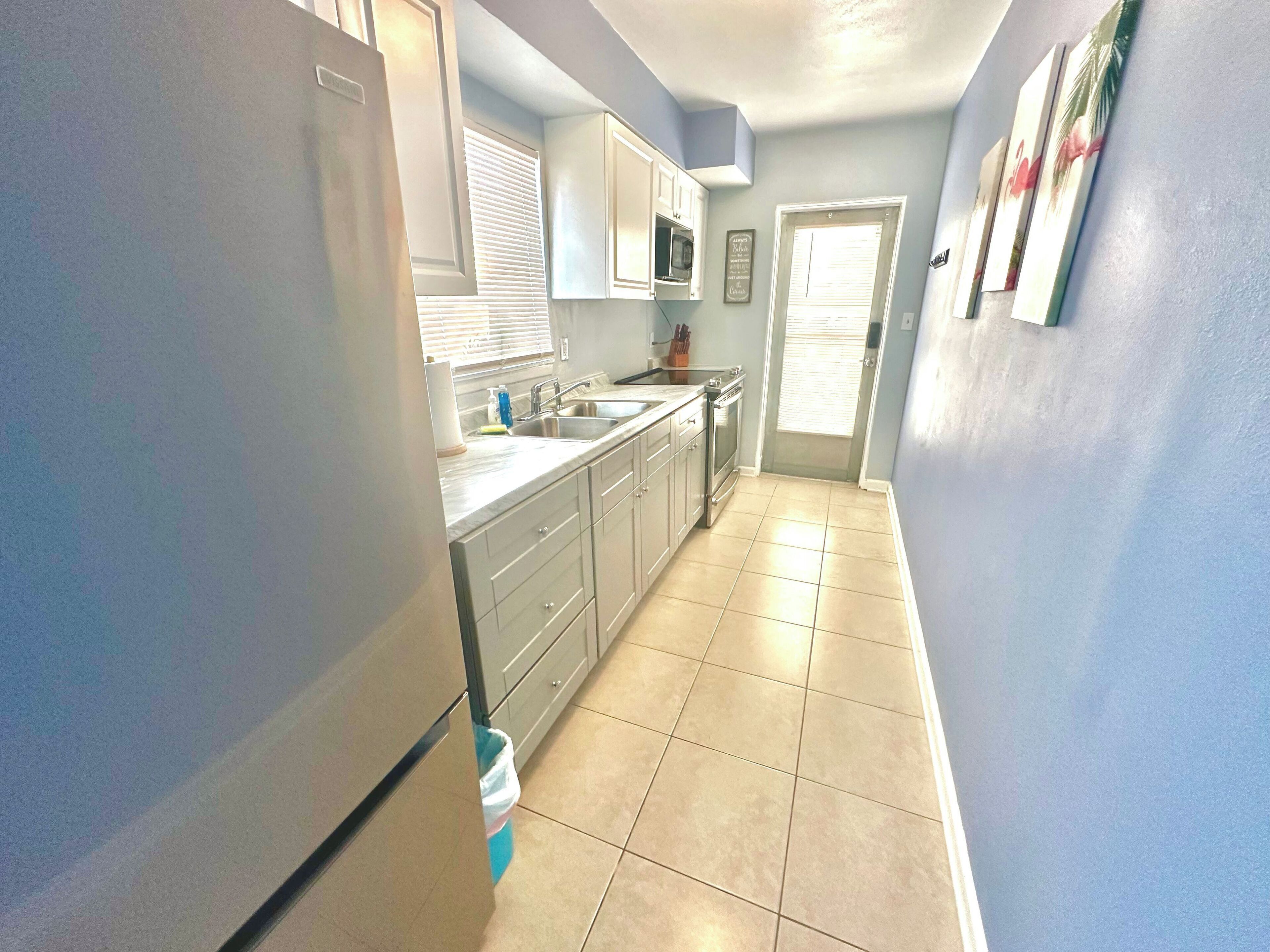 A narrow kitchen with white cabinets, a stainless steel refrigerator, and a microwave.