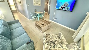 A living room with a grey sofa, a patterned armchair, a wooden coffee table, and a TV displaying an underwater scene.