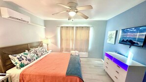 A bedroom with a bed, a TV, a ceiling fan, and a window with curtains.