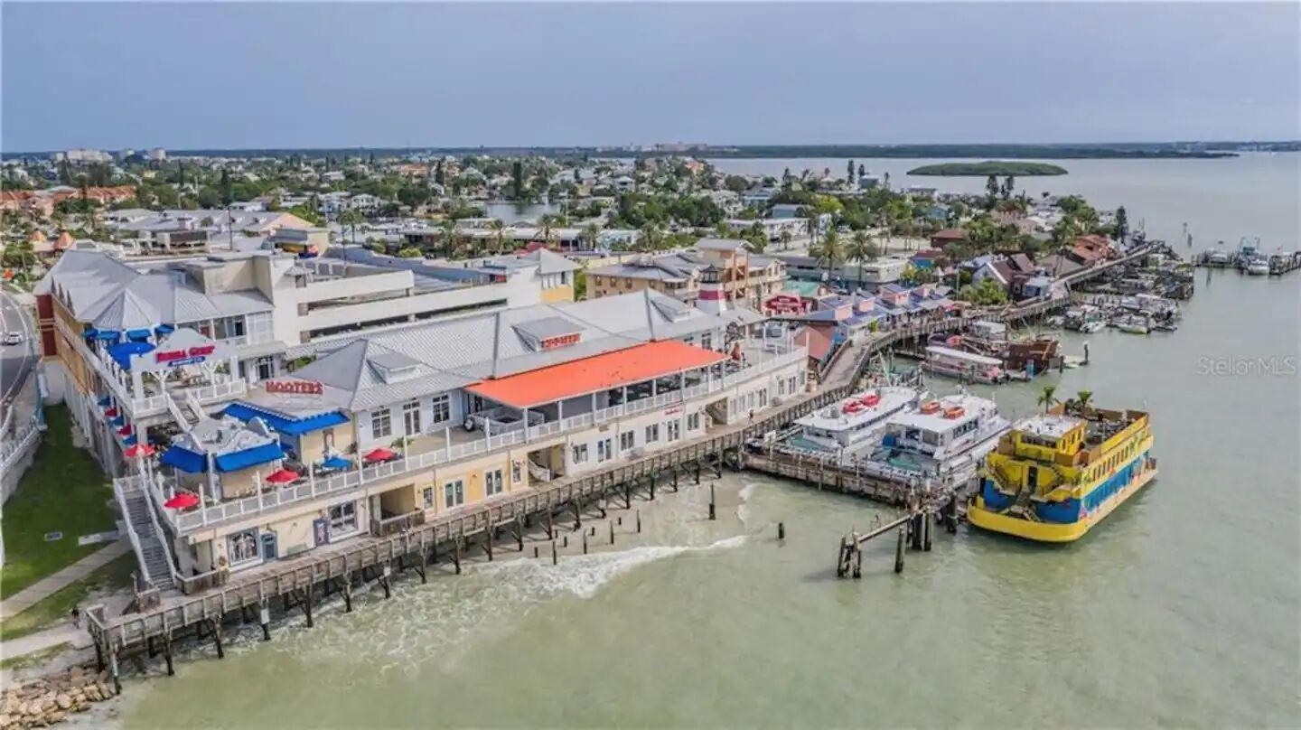 Un hôtel situé au bord de l’eau, doté d’une jetée qui s’avance sur l’eau, d’un grand bateau amarré à la jetée et offrant une vue sur le paysage urbain environnant.