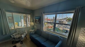 A living room with a blue sofa, a patterned armchair, a small table, and a window with a view of a marina.