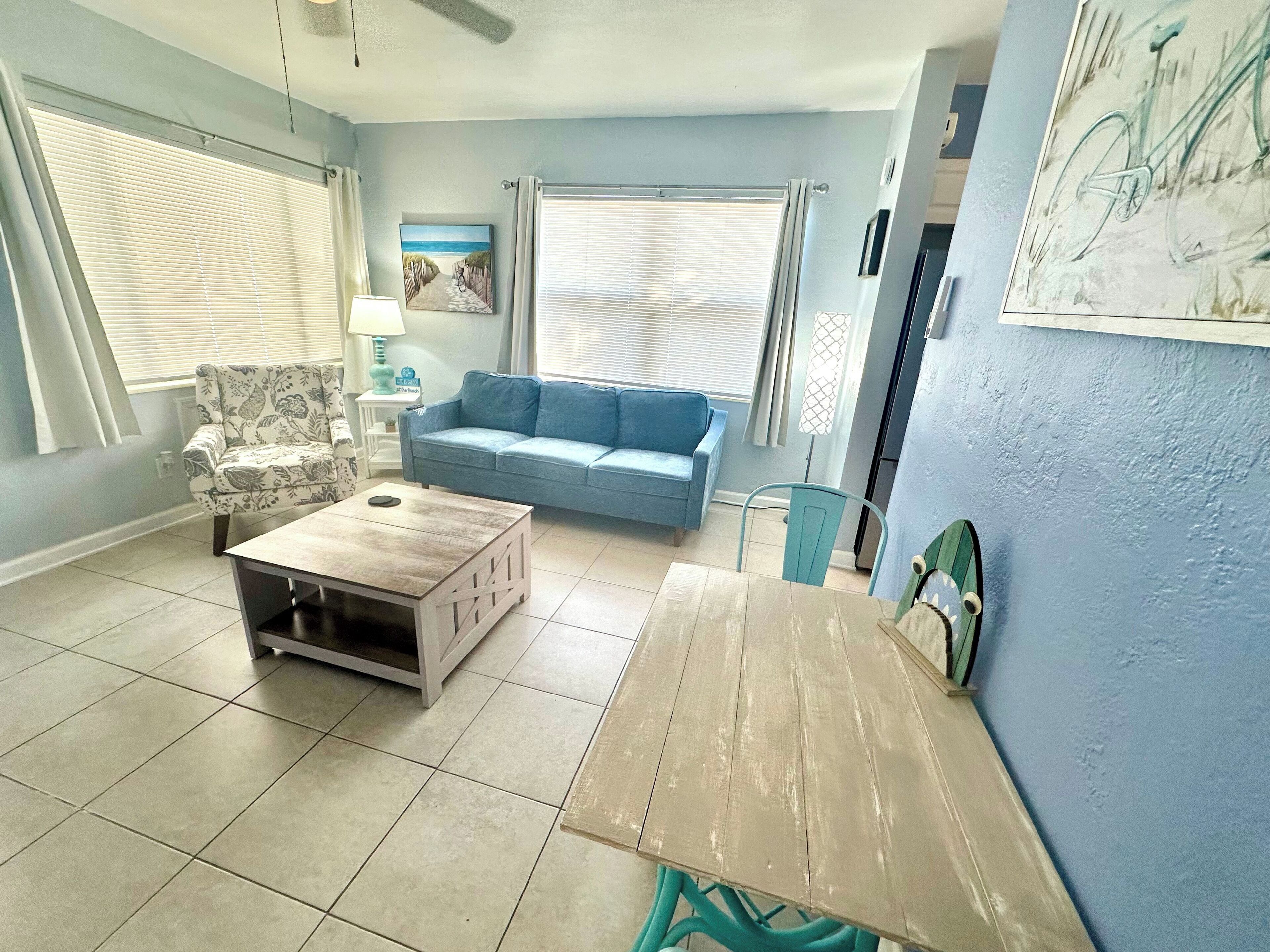 Uma sala de estar com um sofá azul, uma poltrona floral, uma mesa de centro de madeira e um quadro na parede.
