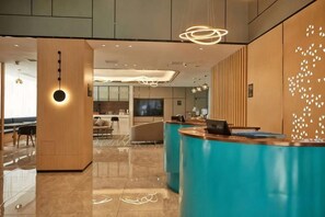 Un hall d’hôtel moderne comprenant un comptoir d’accueil, un espace salon et un écran de télévision.
