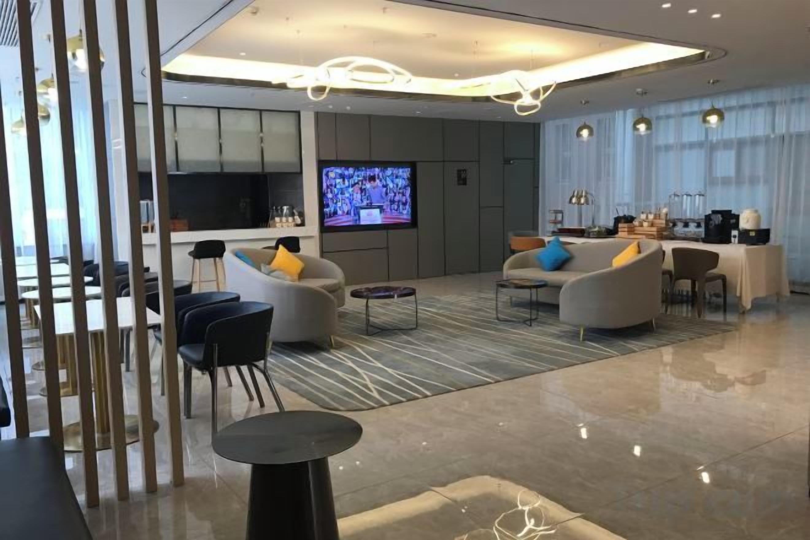Um saguão moderno de hotel, com televisão de tela plana, área de estar e cozinha ao fundo.