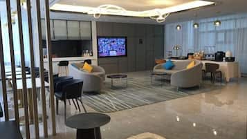 Um saguão moderno de hotel, com televisão de tela plana, área de estar e cozinha ao fundo.