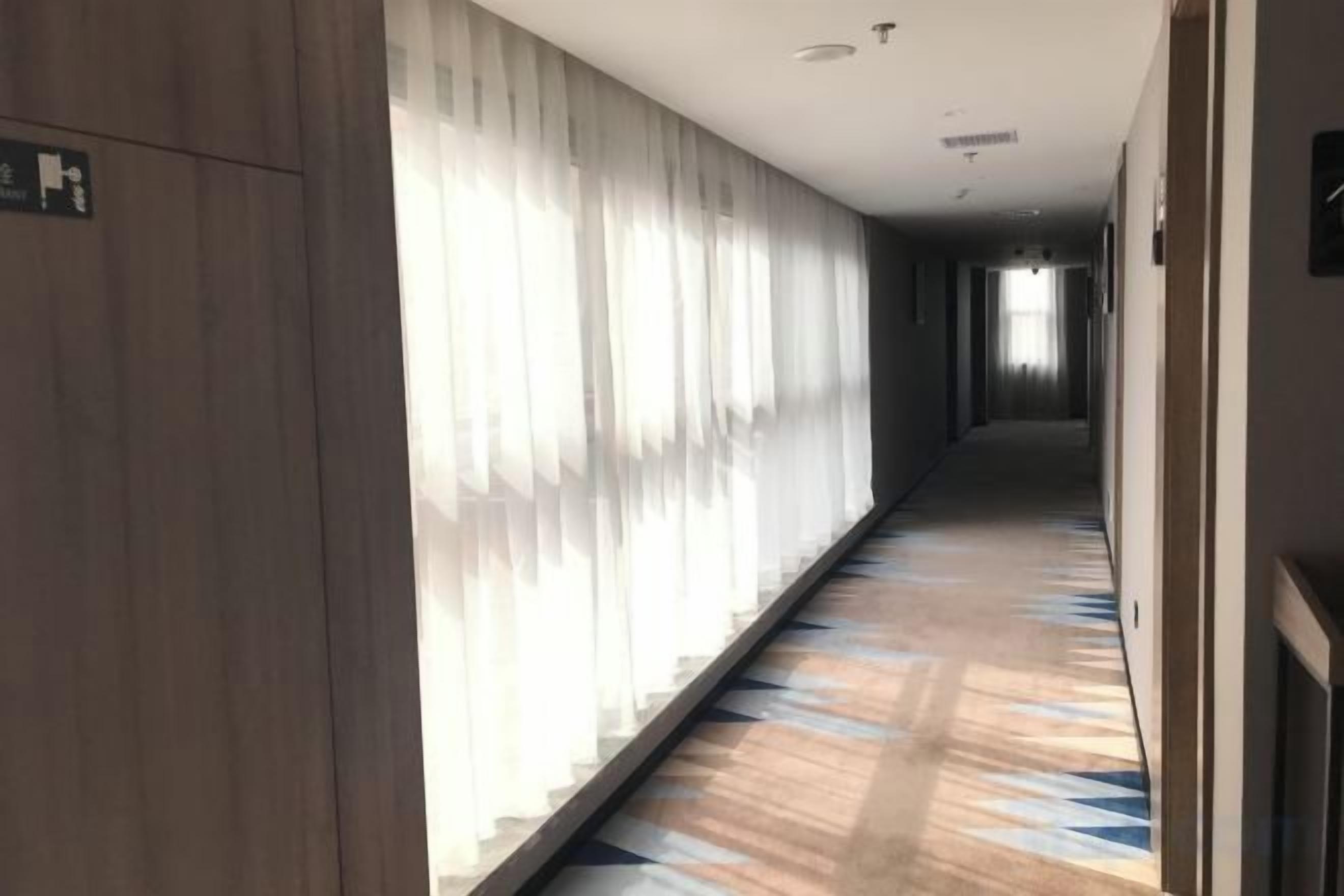 Ein Hotelgang mit einem gemusterten Teppich, Holzvertäfelung und einer langen Gasse, die zu einem hellen Ende führt.