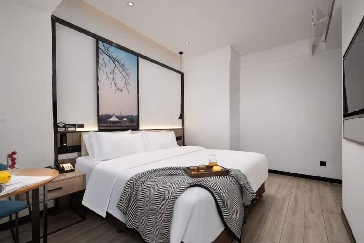 Een hotelkamer met een bed, nachtkastje, lamp en uitzicht op een gebouw.