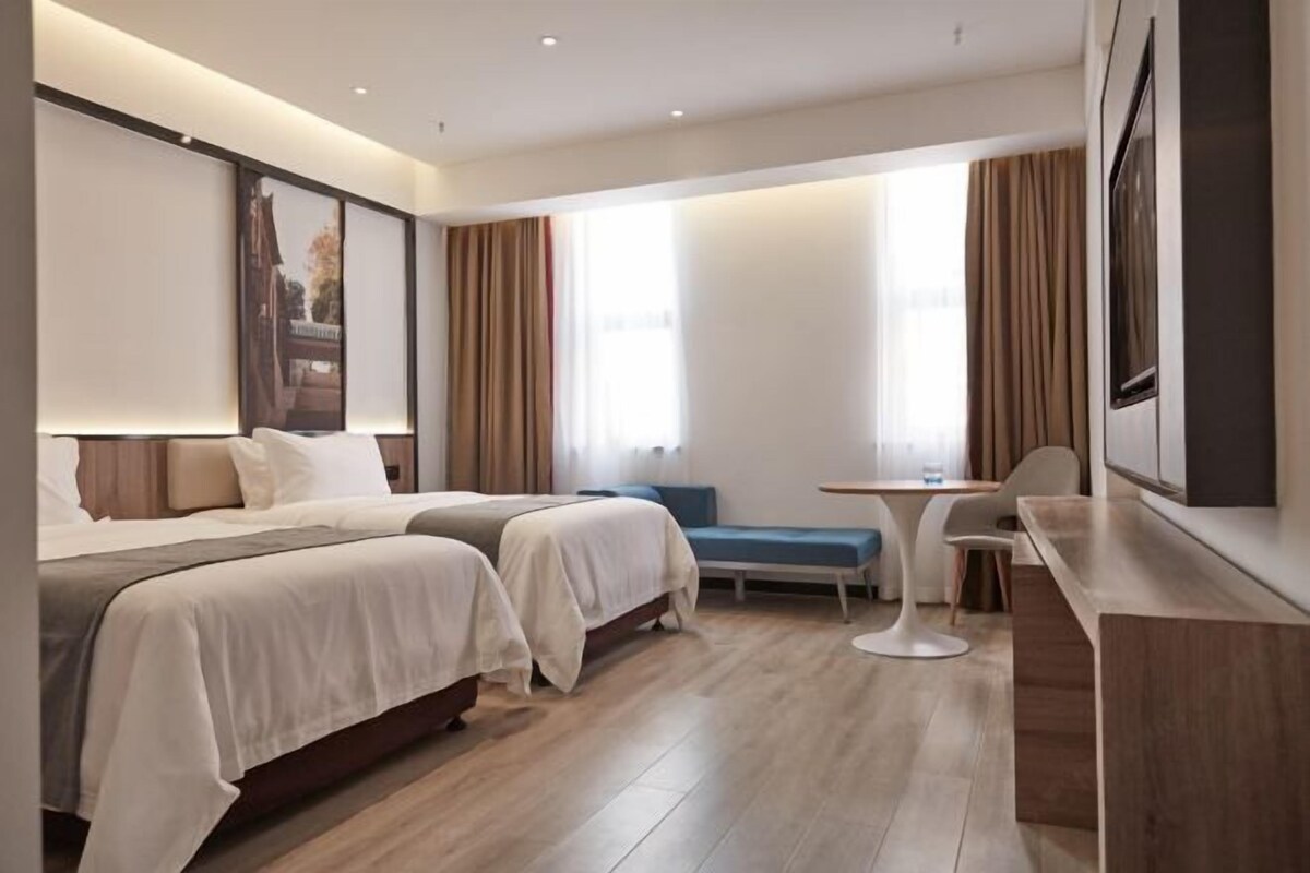 A hotel room with two beds, a desk, a chair, and a small table.