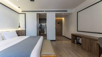 Una habitación de hotel moderna con una cama grande, un banco, un escritorio y un proyector.