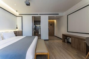 A modern hotel room with a large bed, a bench, a desk, and a projector.