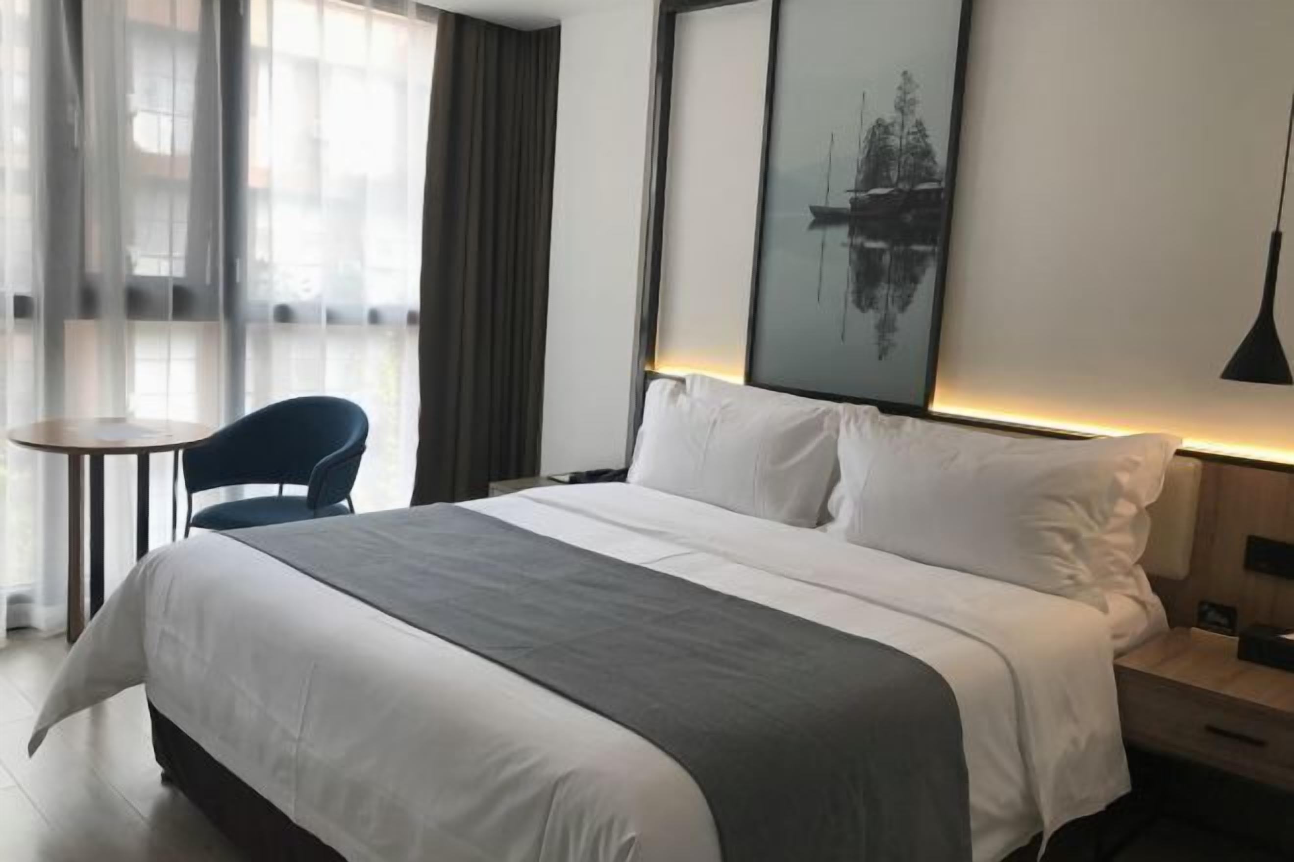 A hotel room with a large bed, a bedside table, a chair, and a window with curtains.