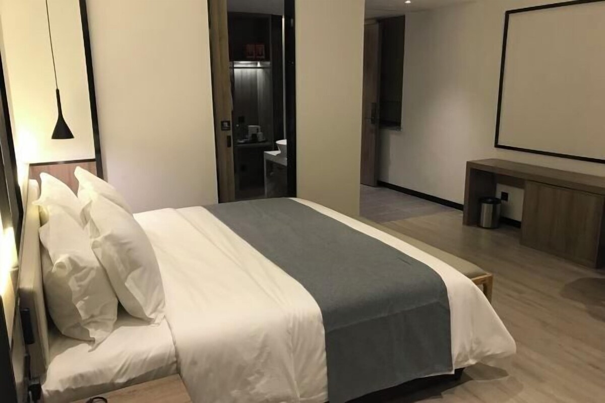 A modern hotel room with a neatly made bed, a bedside table, and a large window.