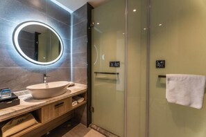 A modern bathroom with a round mirror, a sink, a glass shower enclosure, and a towel rack.