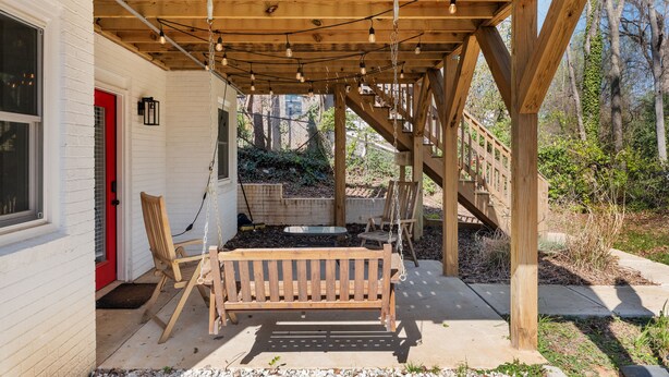 A wooden deck with a swing set and a bench, a red door, and a view of a garden and trees. - Quaint & cozy living minutes from downtown Raleigh (Raleigh)