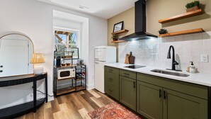 A modern kitchen with a white countertop, green cabinets, and a black range hood. There is a window with a view of trees, a microwave, and a coffee maker on the counter. - Quaint & cozy living minutes from downtown Raleigh (Raleigh)