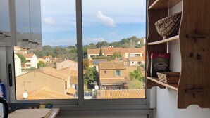 A kitchen with a large window, wooden cabinets, a sink, and a trash bin. - Spacious & comfortable T2 air-conditioned 3* Wifi, Private parking, Beach 100m (Saint-Mandrier-sur-Mer)