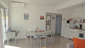A modern kitchen with white cabinets, a microwave, and a stove. There is a dining area with a table and chairs, and a sofa with an orange cushion. - Spacious & comfortable T2 air-conditioned 3* Wifi, Private parking, Beach 100m (Saint-Mandrier-sur-Mer)