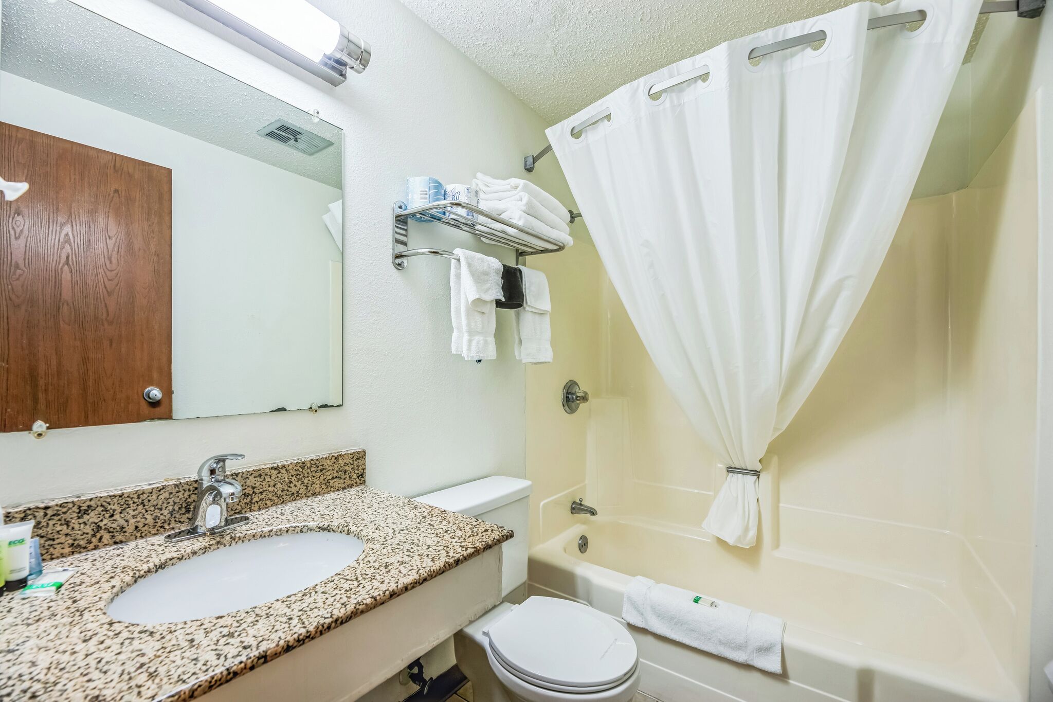 A bathroom with a granite countertop sink, a toilet, a bathtub, and a shower curtain.
