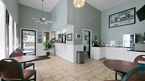 A spacious room with a high ceiling, a ceiling fan, a kitchenette, and a dining area with red upholstered chairs. - Hotel 8 (Fergus Falls)