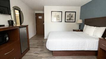 Habitación de hotel con cama, escritorio con computadora, espejo y dos cuadros en la pared.