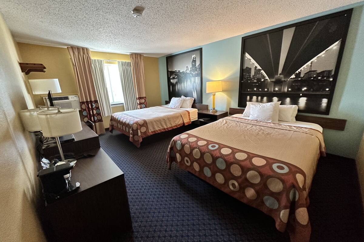 Une chambre d’hôtel avec deux lits, un bureau avec une lampe, une fenêtre avec des rideaux et une vue sur la ville.